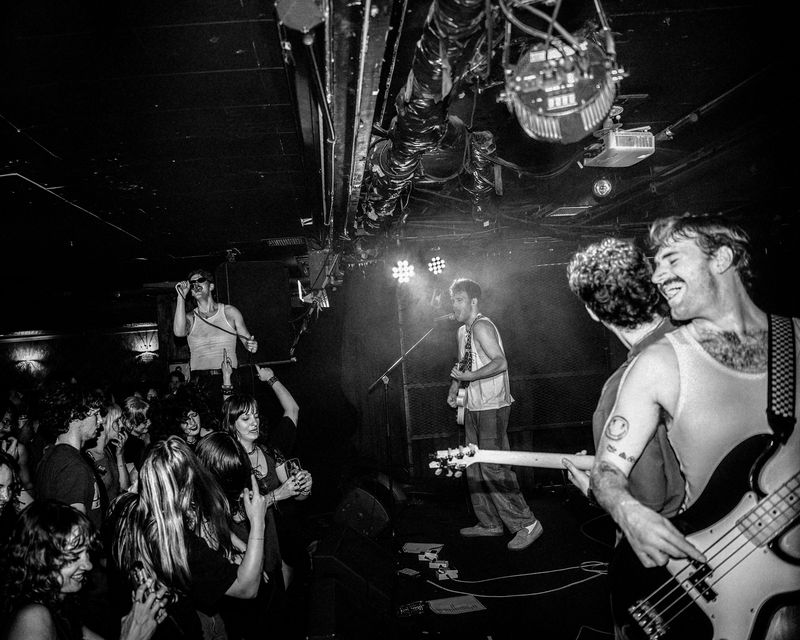 Dirty Aesthetic plays to a dancing crowd, grinning bassist up front, singer in sunglasses raised above them, black and white